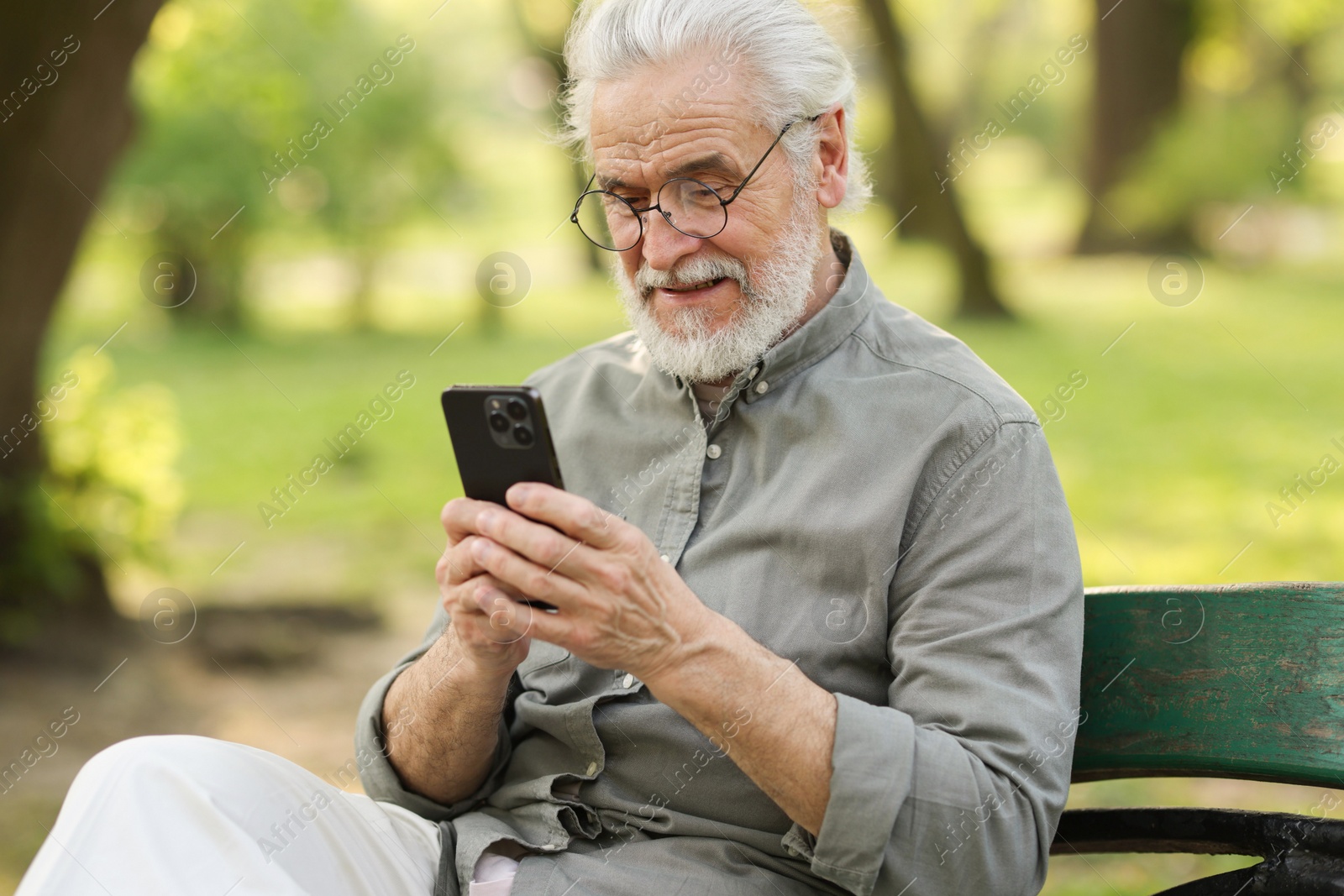 Photo of Portrait of happy grandpa with glasses using smartphone on bench in park