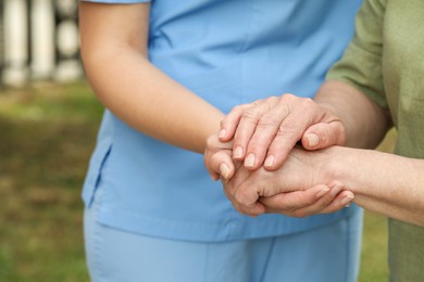 Photo of Elderly woman and female caregiver holding hands outdoors, closeup