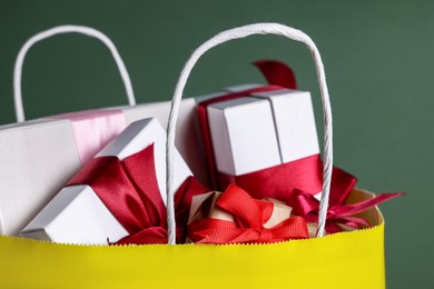 Photo of Yellow paper shopping bag full of gift boxes on green background, closeup