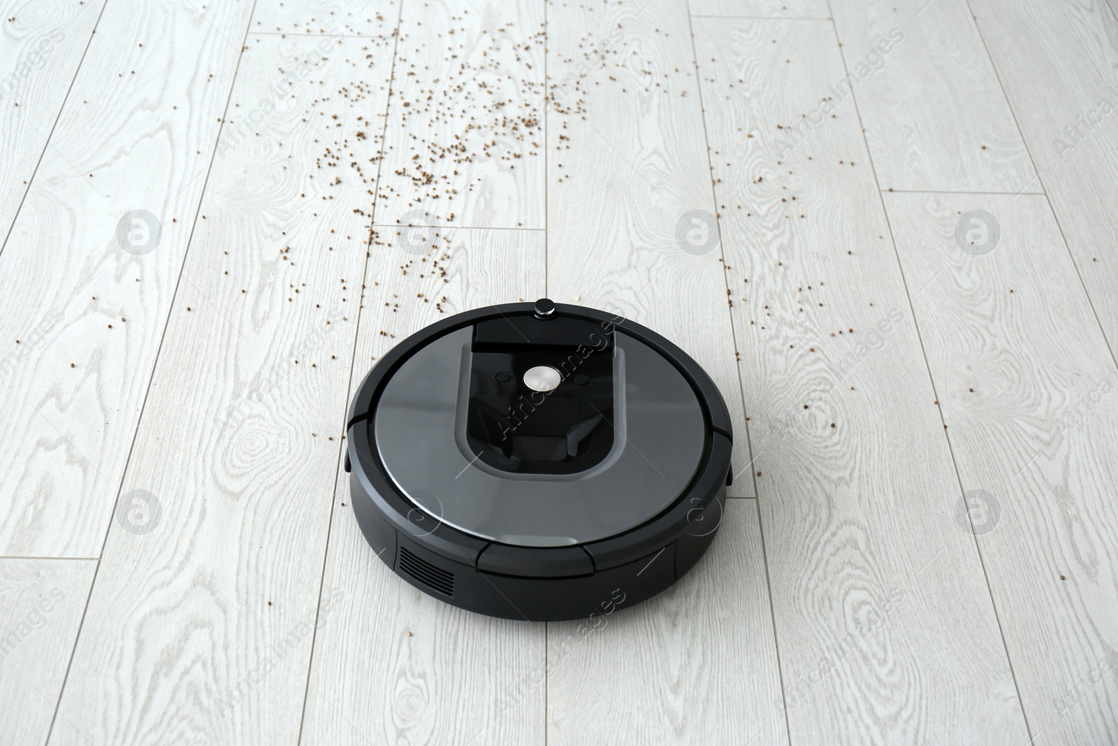 Photo of Modern robotic vacuum cleaner removing scattered buckwheat from wooden floor