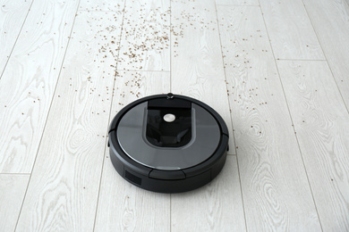 Modern robotic vacuum cleaner removing scattered buckwheat from wooden floor