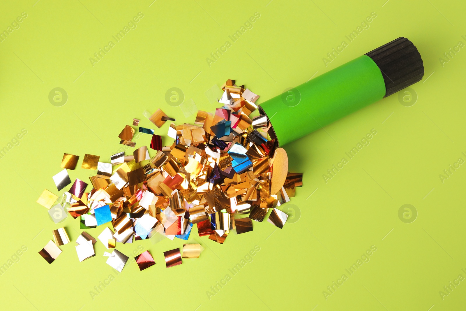 Photo of Shiny colorful confetti bursting out of party popper on green background, flat lay