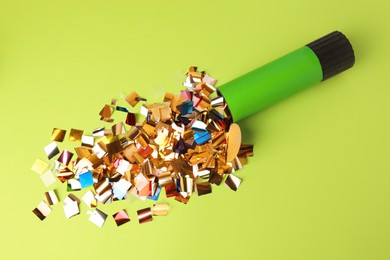 Photo of Shiny colorful confetti bursting out of party popper on green background, flat lay