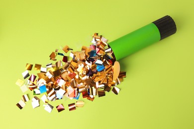 Shiny colorful confetti bursting out of party popper on green background, flat lay