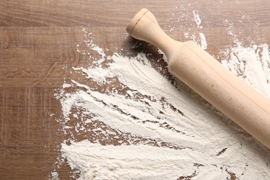 Photo of Scattered flour and rolling pin on wooden table, top view