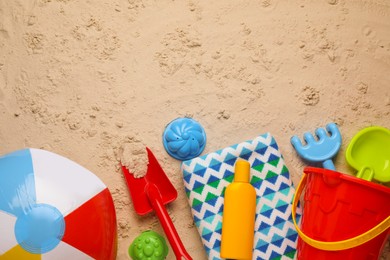 Photo of Colorful inflatable ball, plastic beach toys, sunscreen and blanket on sand, flat lay. Space for text