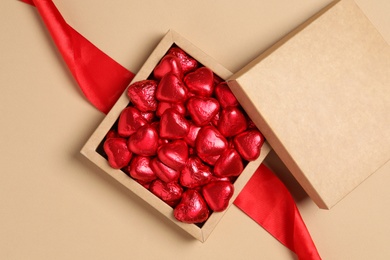 Beautiful heart shaped chocolate candies in box on beige background, flat lay