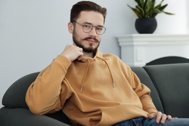 Serious man sitting on grey sofa in cozy room