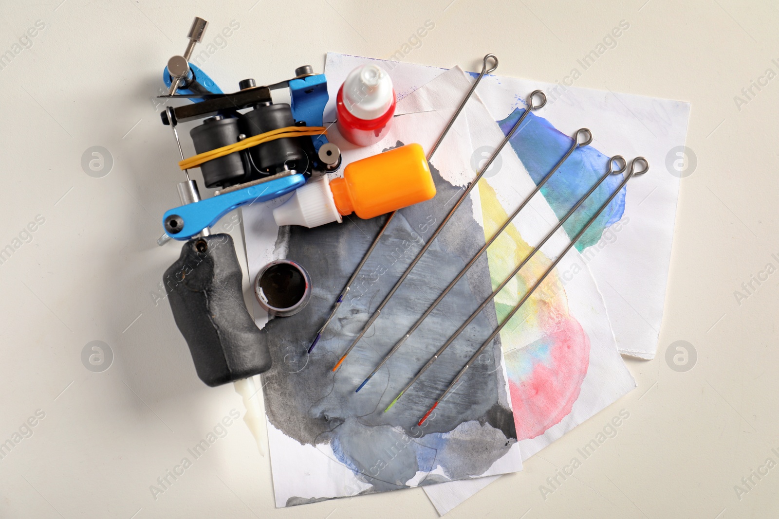 Photo of Tattoo machine, needles, ink and sheets of paper on white background, top view