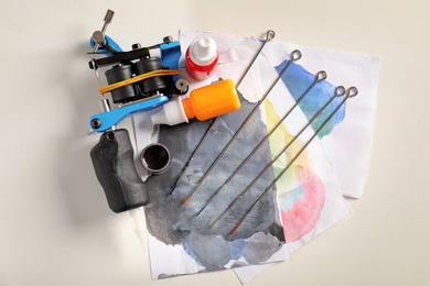 Tattoo machine, needles, ink and sheets of paper on white background, top view