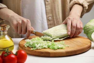 Photo of Woman cutting fresh chinese cabbage at white wooden table, closeup