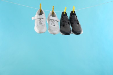 Photo of Different stylish sneakers drying on washing line against light blue background, space for text