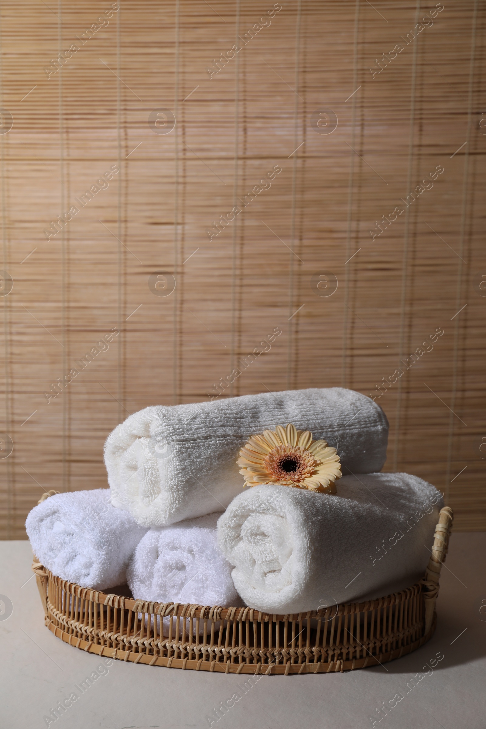 Photo of Rolled terry towels and flower on white table indoors, space for text