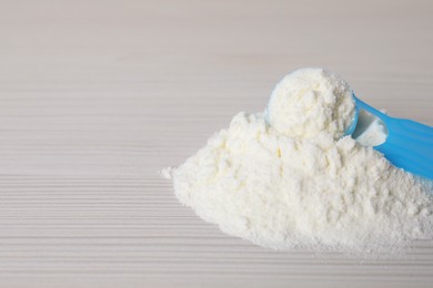 Photo of Powdered infant formula and scoop on white wooden table, closeup with space for text. Baby milk