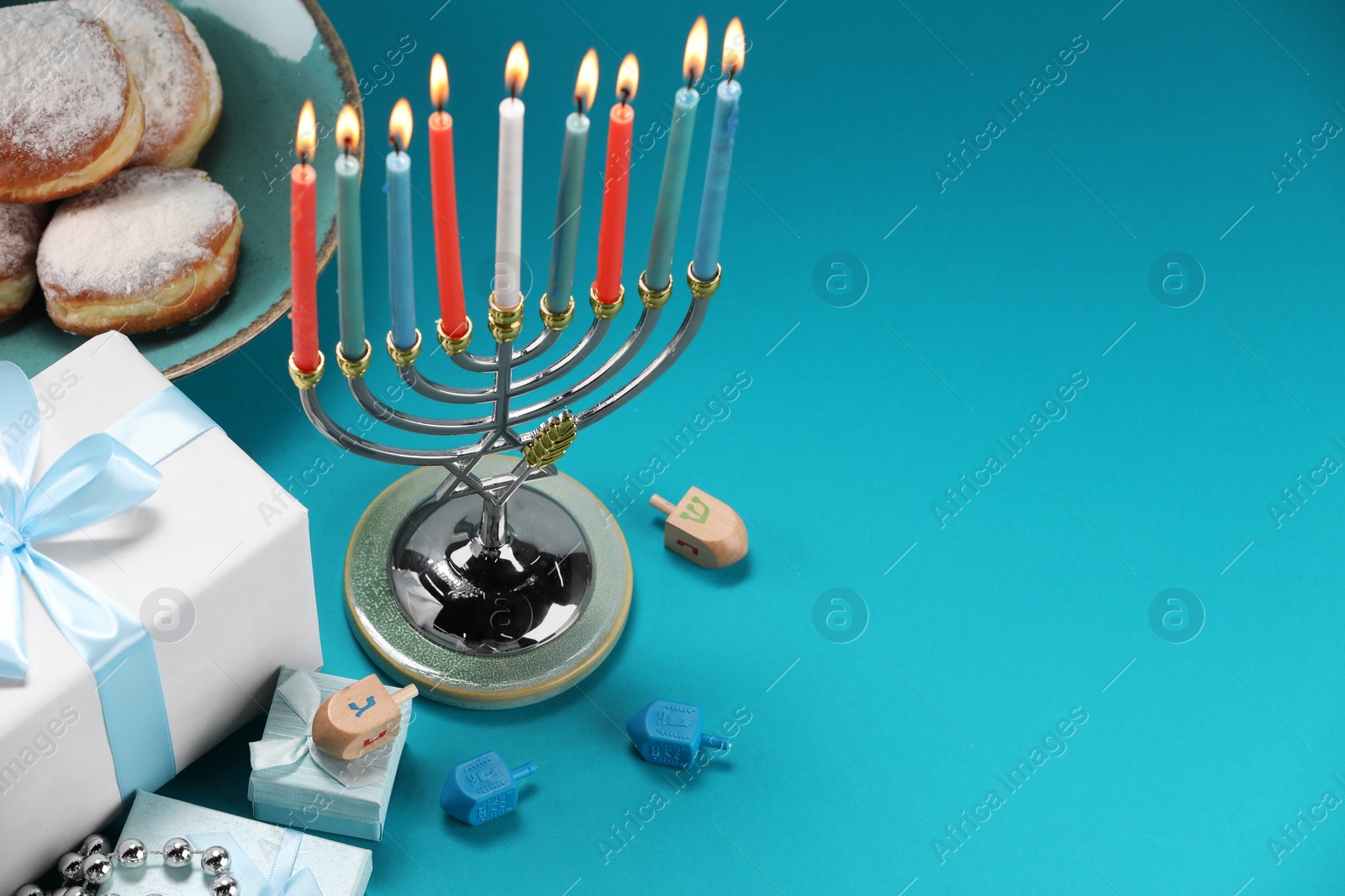 Photo of Hanukkah celebration. Menorah with burning candles, dreidels, donuts and gift boxes on blue table, above view. Space for text