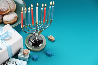 Hanukkah celebration. Menorah with burning candles, dreidels, donuts and gift boxes on blue table, above view. Space for text