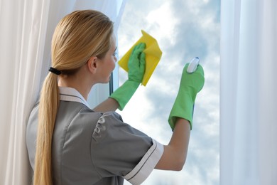 Chambermaid cleaning window with rag indoors, back view