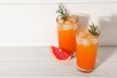 Photo of Tasty grapefruit drink with ice and rosemary in glasses on white wooden table. Space for text