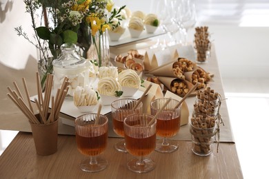 Photo of Delicious treats and glasses of drink on wooden table in room. Sweet buffet