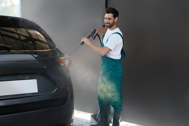 Photo of Worker washing auto with high pressure water jet at outdoor car wash