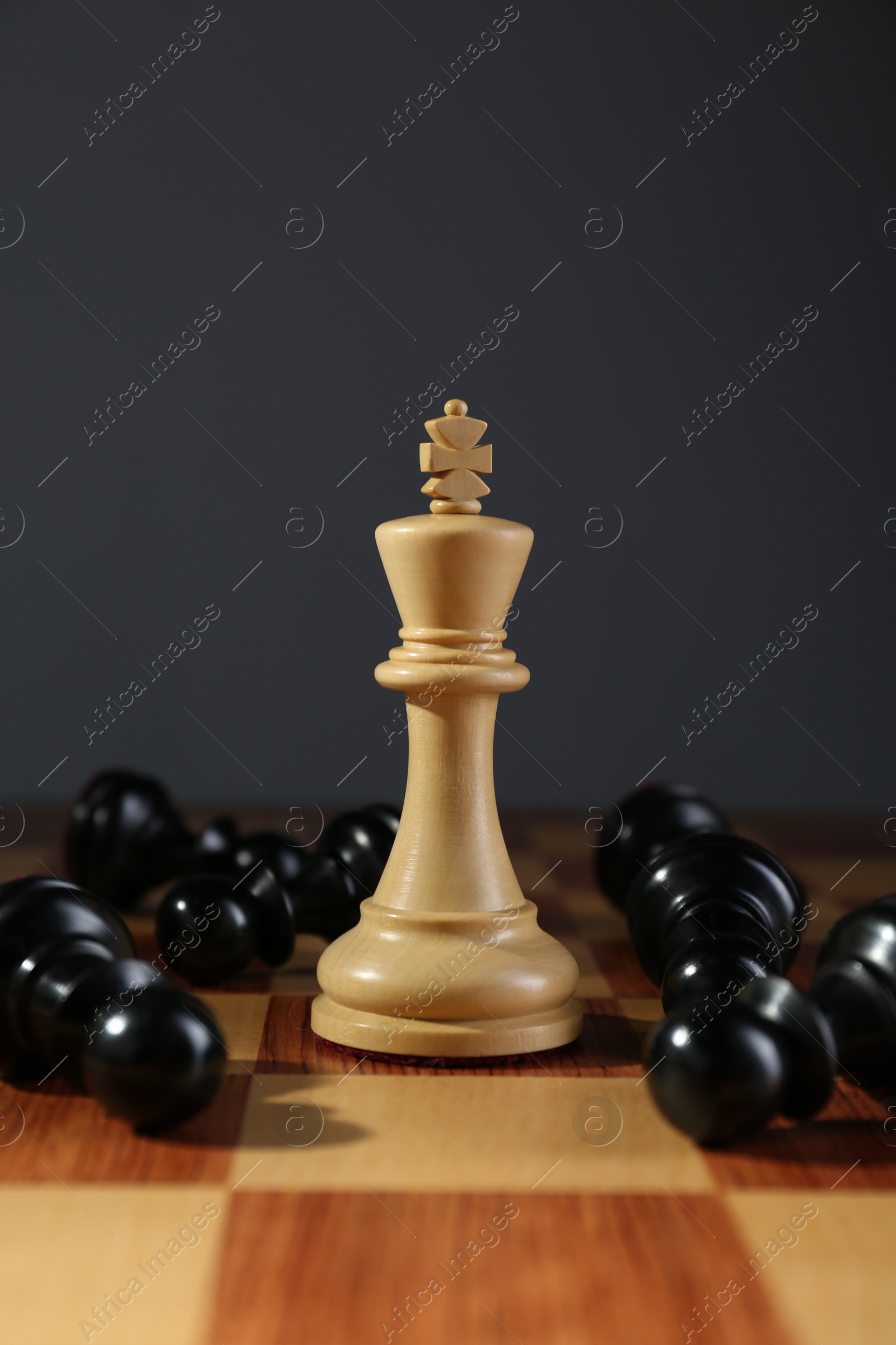 Photo of King among fallen black chess pieces on wooden board against dark background. Competition concept