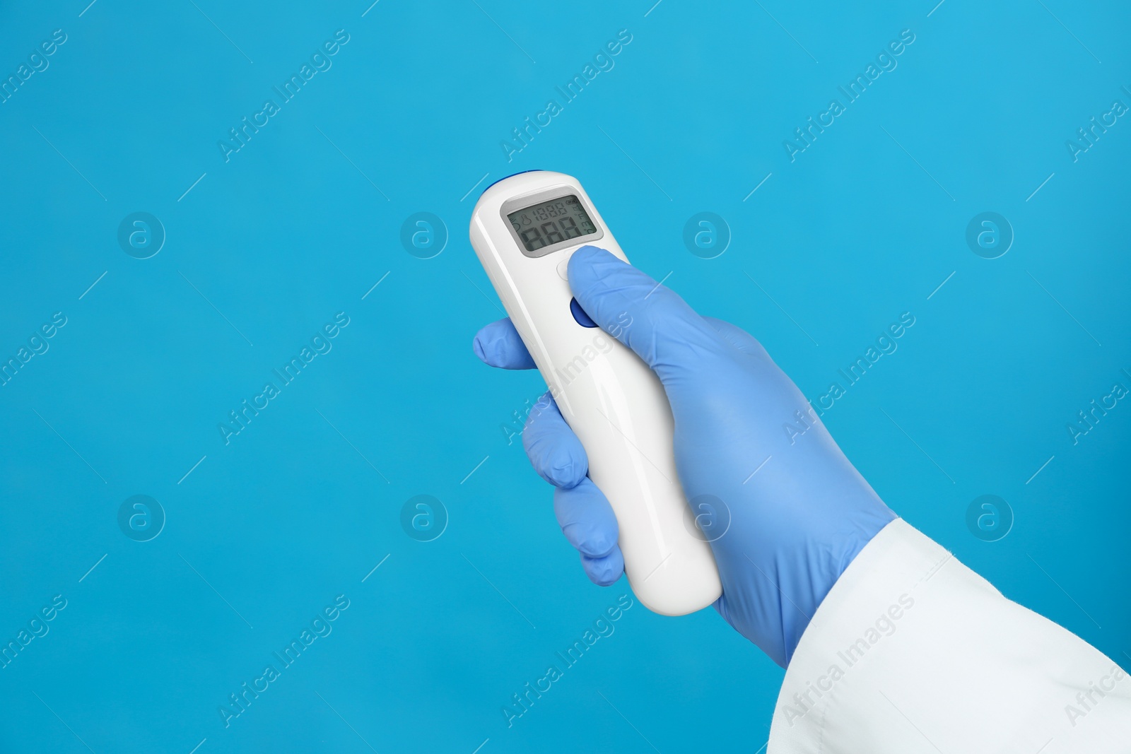 Photo of Doctor holding non contact infrared thermometer on light blue background, closeup. Measuring temperature