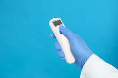 Photo of Doctor holding non contact infrared thermometer on light blue background, closeup. Measuring temperature