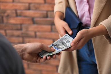 Photo of Man giving woman American money near brick wall, closeup