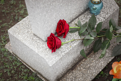 Red roses and candle on old grey tombstone outdoors. Funeral ceremony