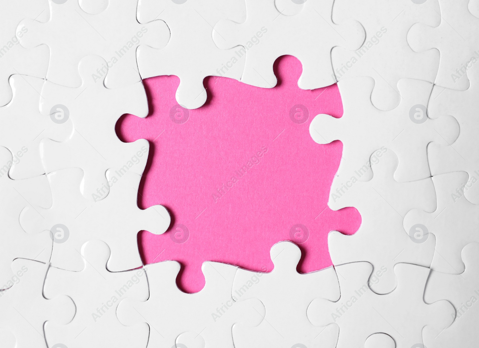 Photo of Frame made with white puzzle pieces on pink background, top view. Space for text