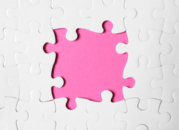 Photo of Frame made with white puzzle pieces on pink background, top view. Space for text