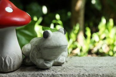 Photo of Frog figure and decorative fly agaric on stone parapet outdoors. Space for text