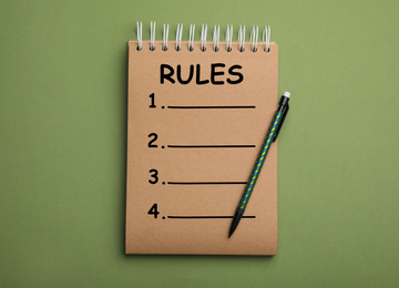 Image of Kraft notebook with list of rules and pencil on green background, top view