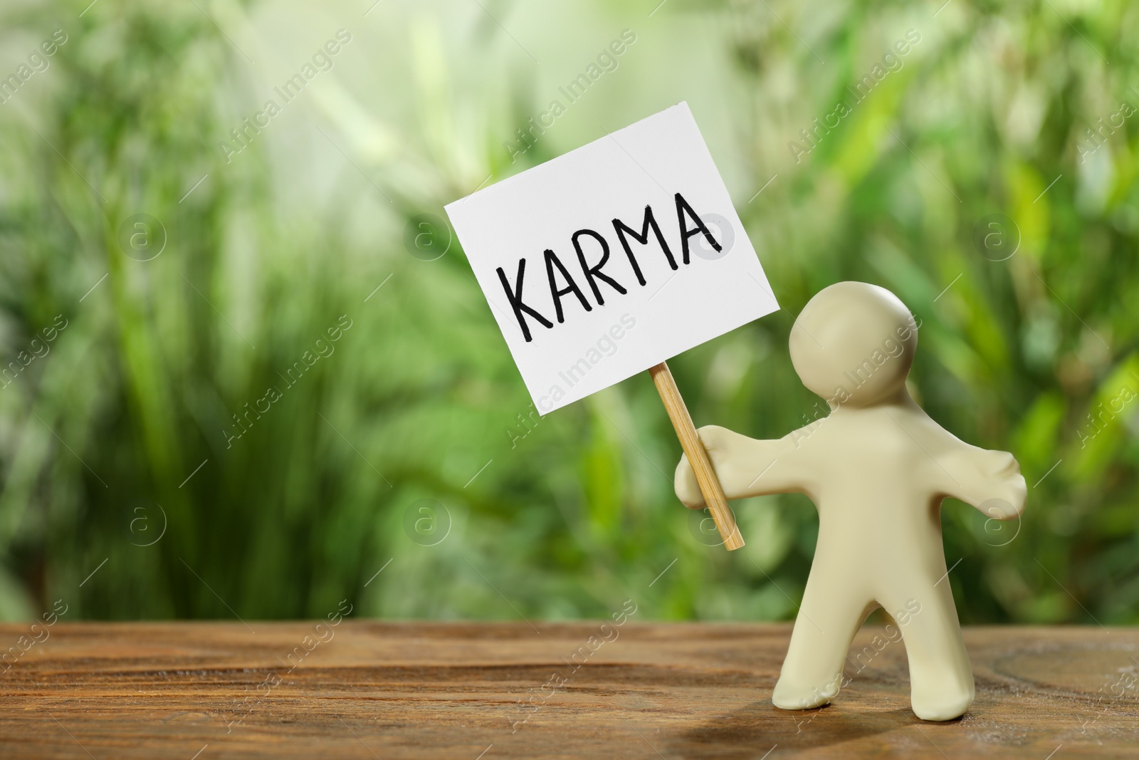 Photo of Human figure holding sign with word Karma on wooden table. Space for text
