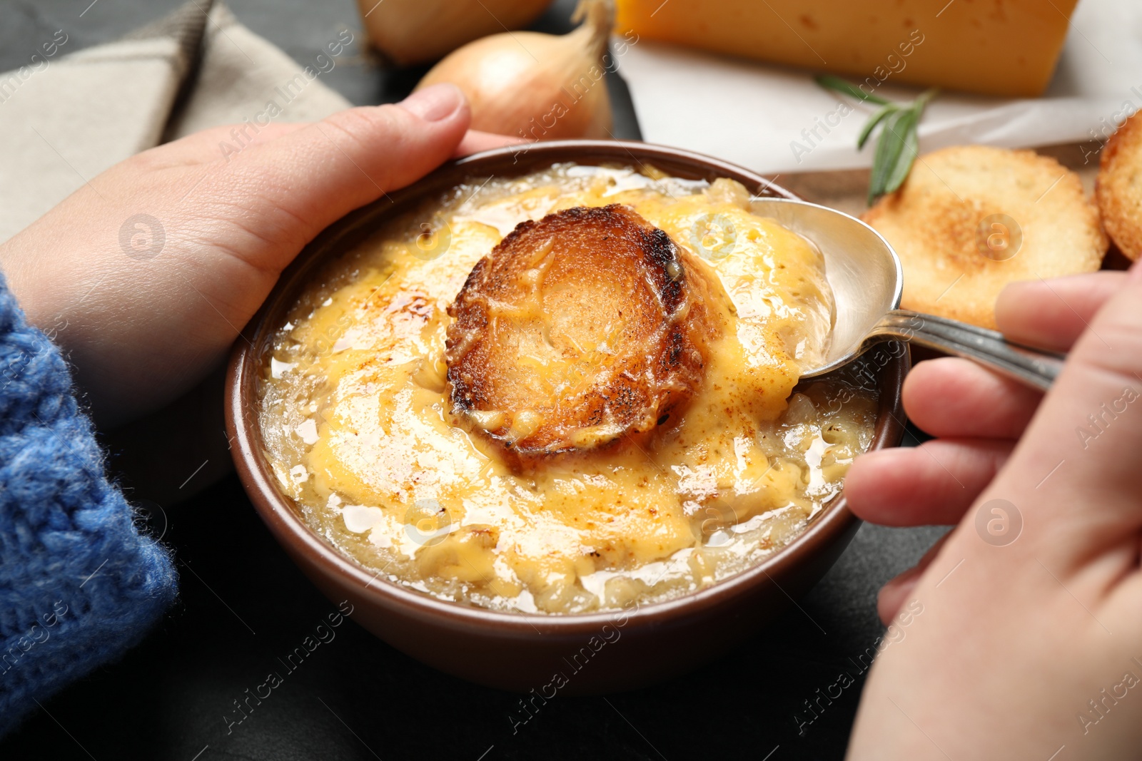 Photo of Woman eating tasty homemade french onion soup at black table, closeup