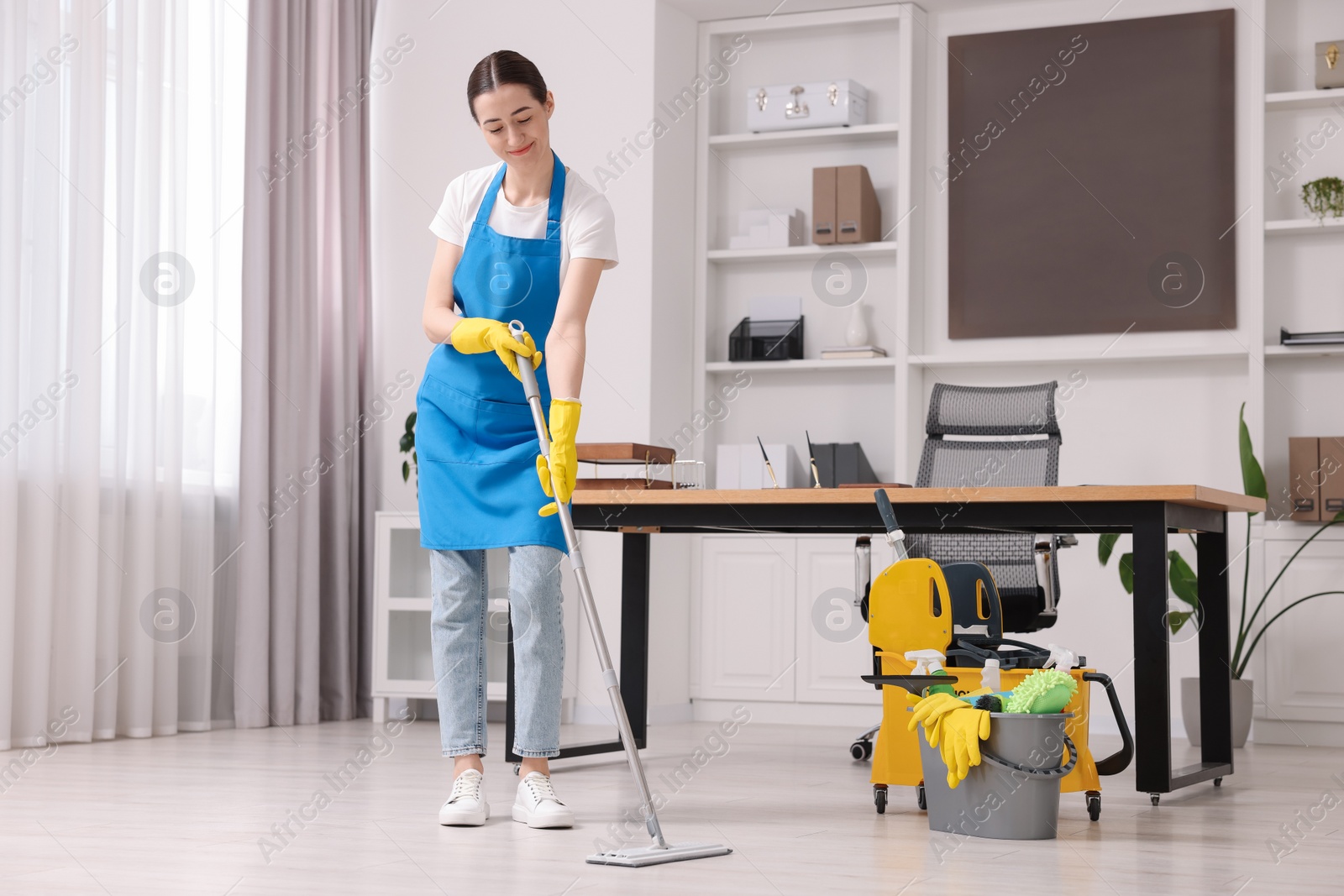 Photo of Cleaning service worker washing floor with mop. Bucket with supplies in office