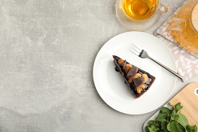 Piece of tasty homemade chocolate cake served with nuts, mint and tea on grey table, flat lay. Space for text