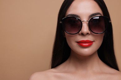 Photo of Attractive woman in fashionable sunglasses against beige background, closeup. Space for text