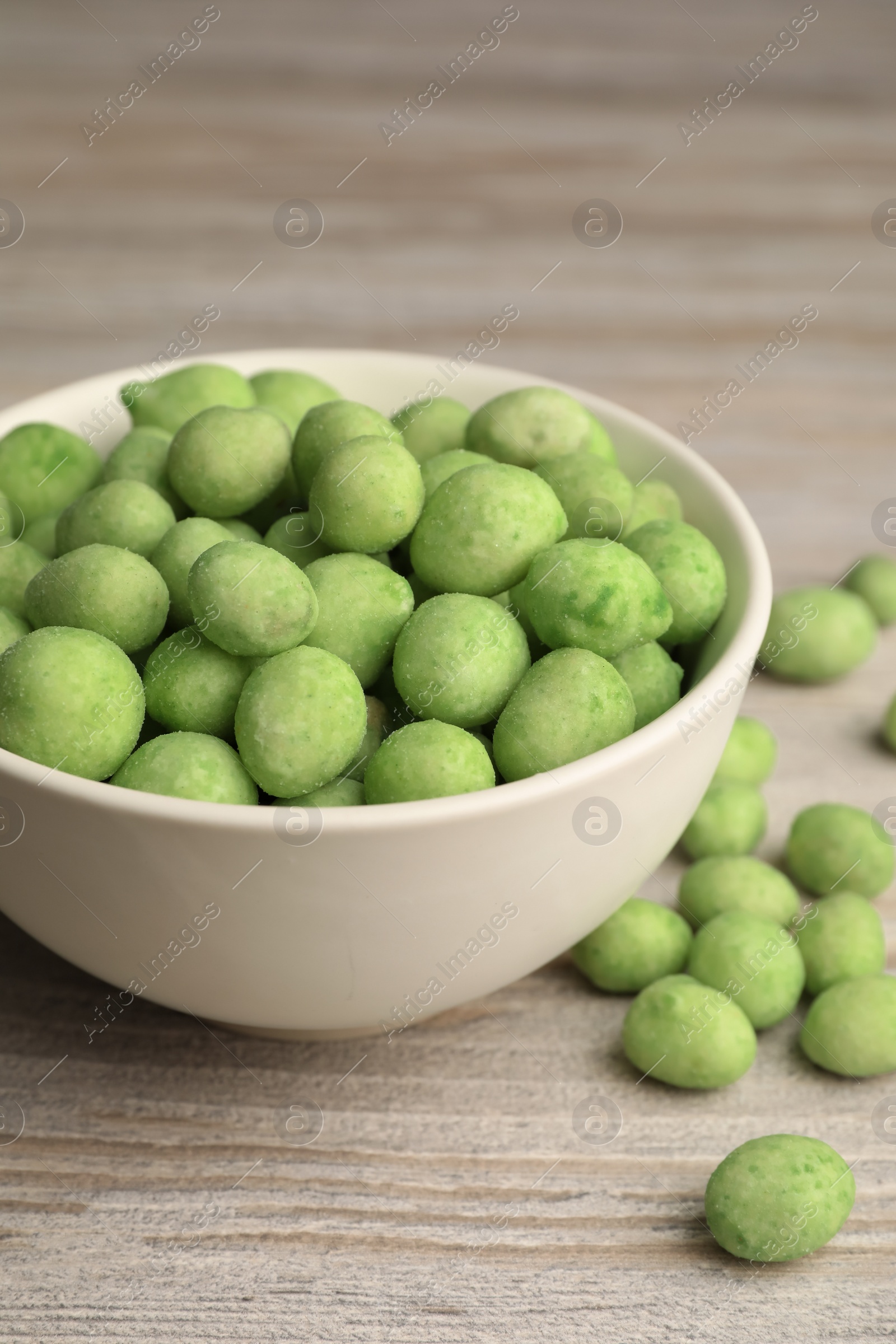 Photo of Bowl with tasty wasabi coated peanuts on white wooden table, closeup