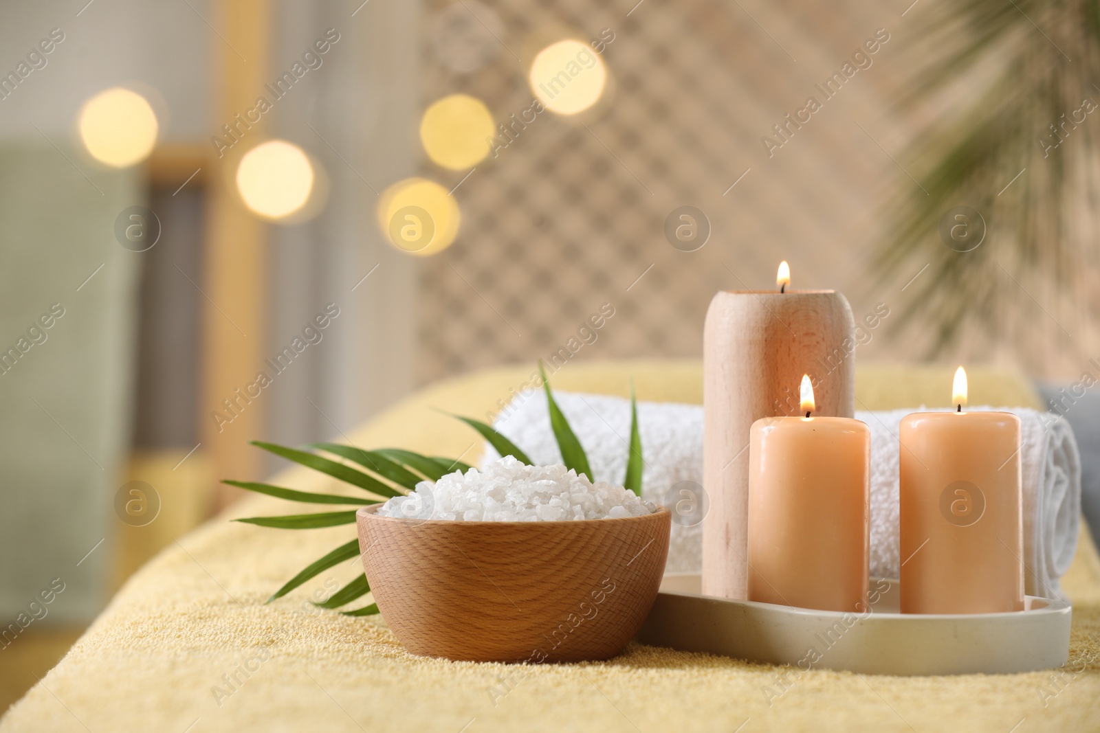 Photo of Spa composition. Burning candles, sea salt and towel on soft yellow surface, space for text