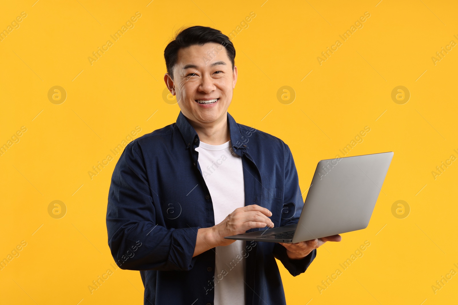 Photo of Portrait of happy man with laptop on yellow background