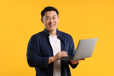 Portrait of happy man with laptop on yellow background