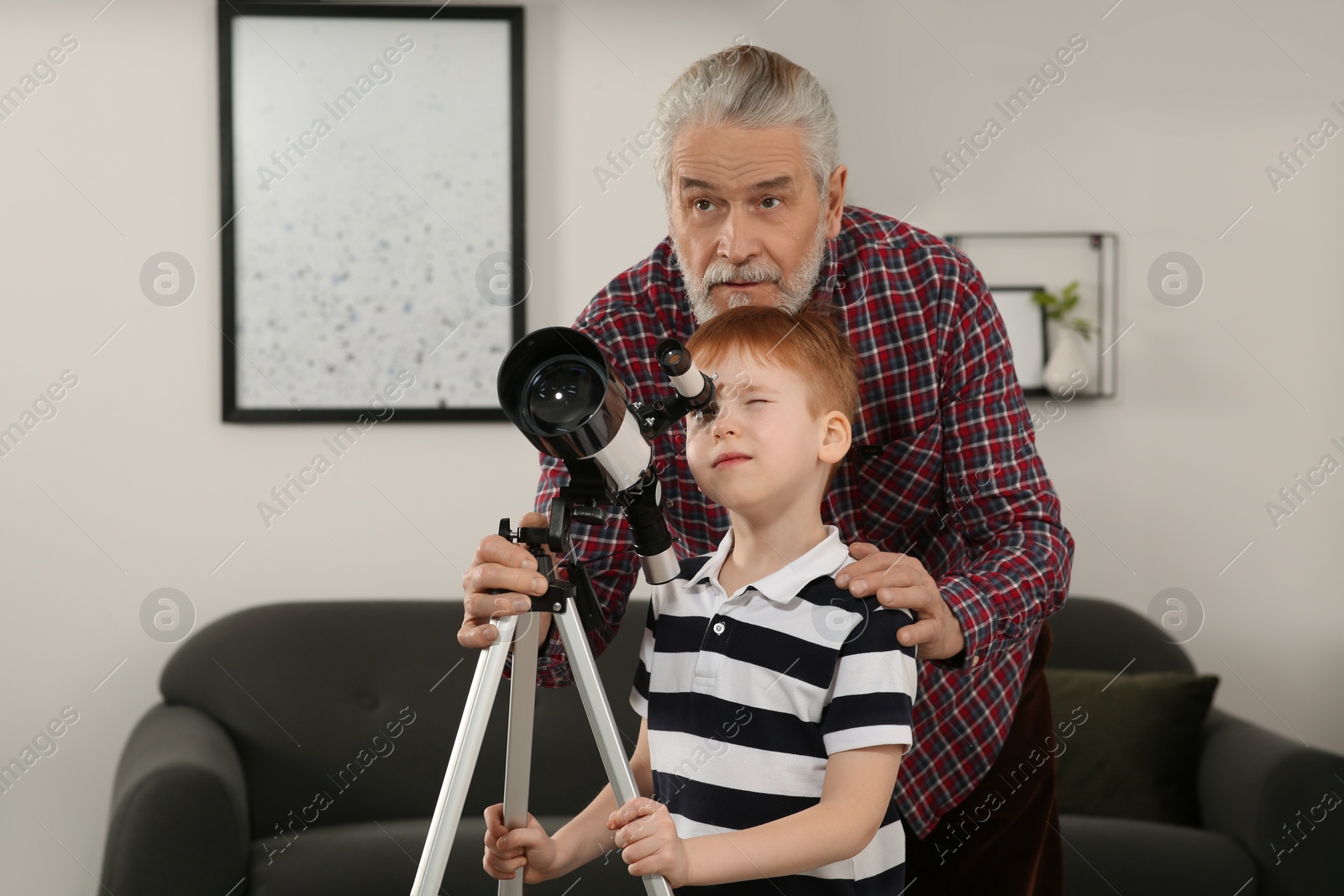 Photo of Little boy with his grandfather looking at stars through telescope in room