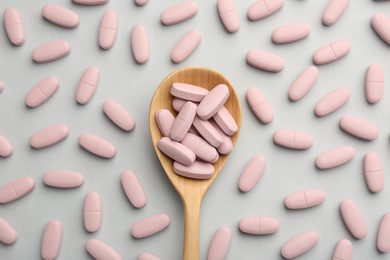 Photo of Vitamin pills and wooden spoon on light grey background, top view. Health supplement