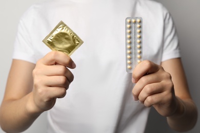 Young woman holding birth control pills and condom, closeup. Safe sex concept