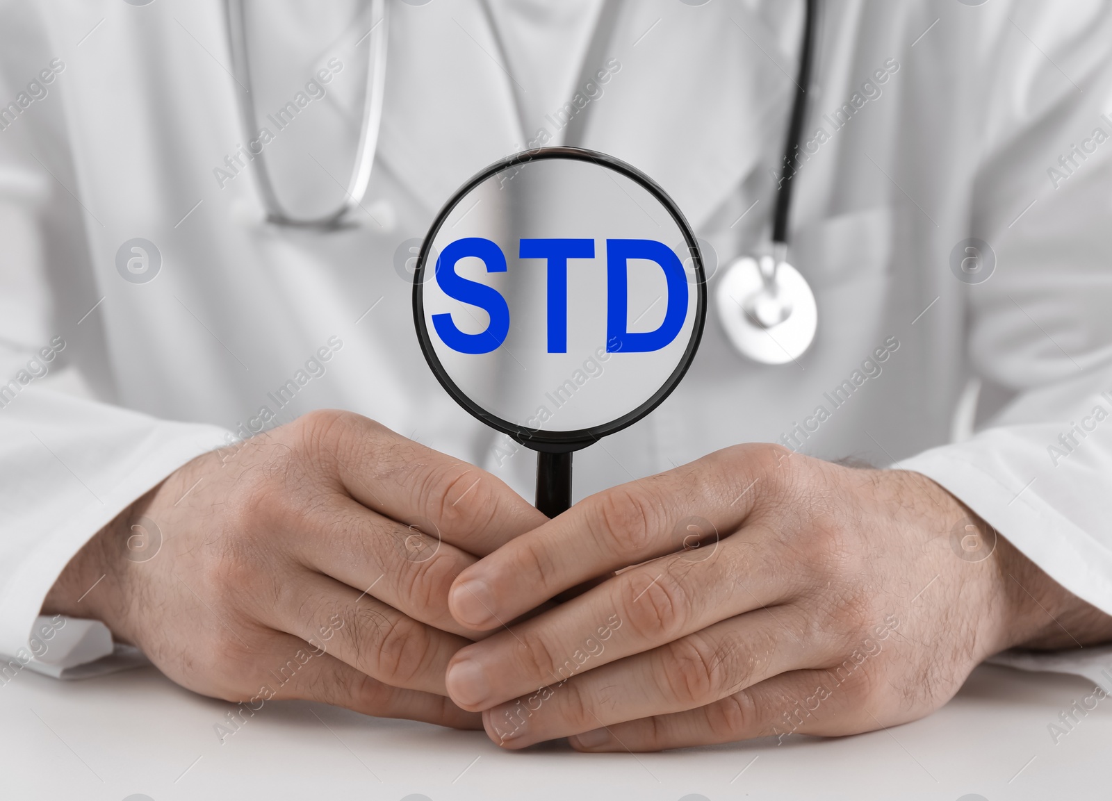 Photo of Doctor holding magnifying glass with abbreviation STD at white table, closeup