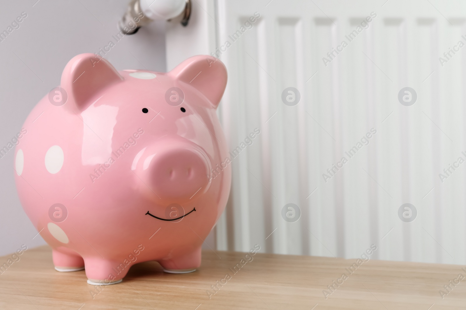 Photo of Piggy bank on wooden table near heating radiator, space for text