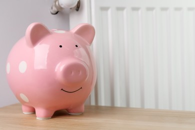 Photo of Piggy bank on wooden table near heating radiator, space for text