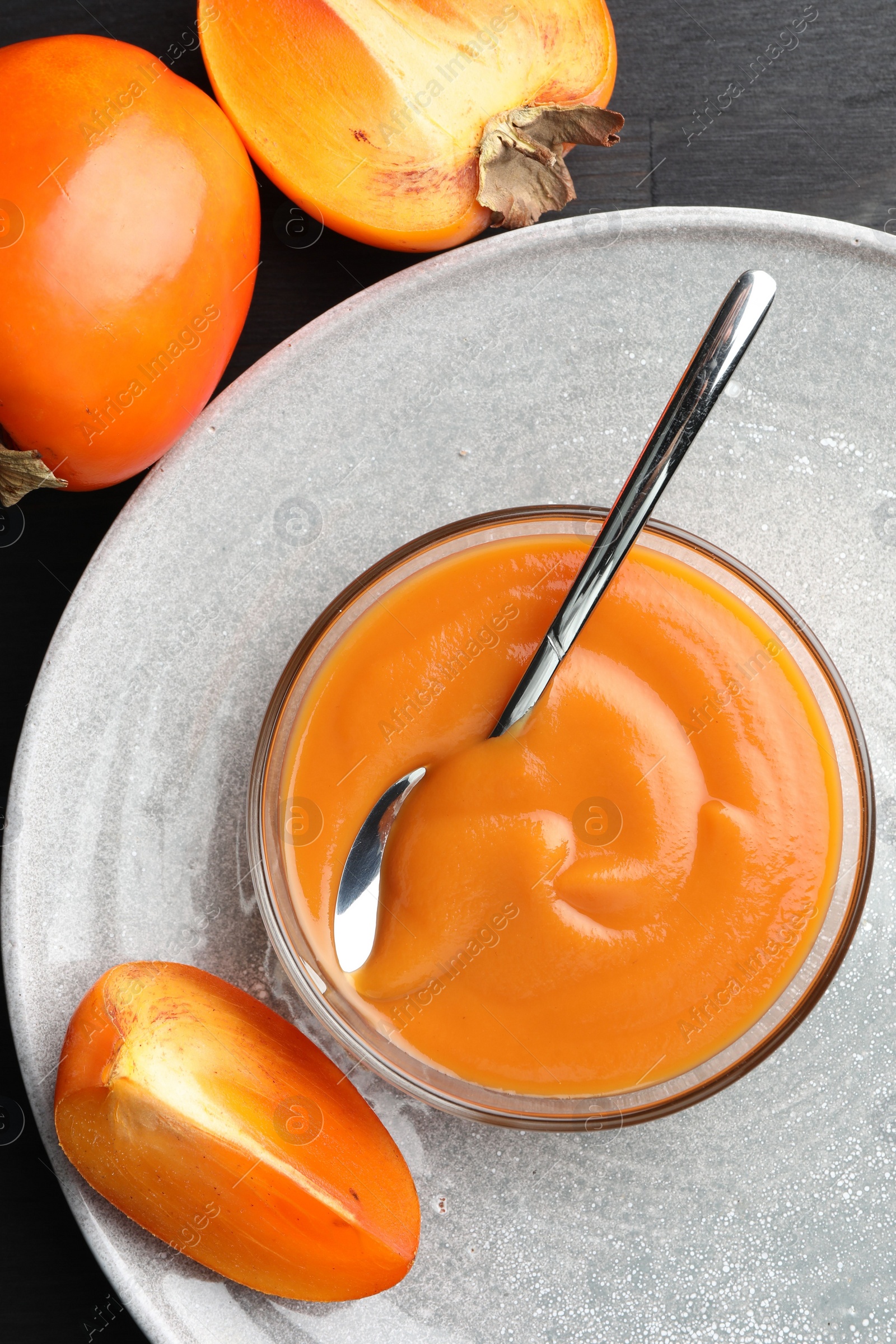 Photo of Delicious persimmon jam in glass bowl served on table, flat lay