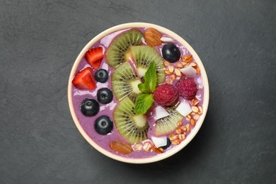 Photo of Delicious acai smoothie with granola and fruits in dessert bowl on black table, top view